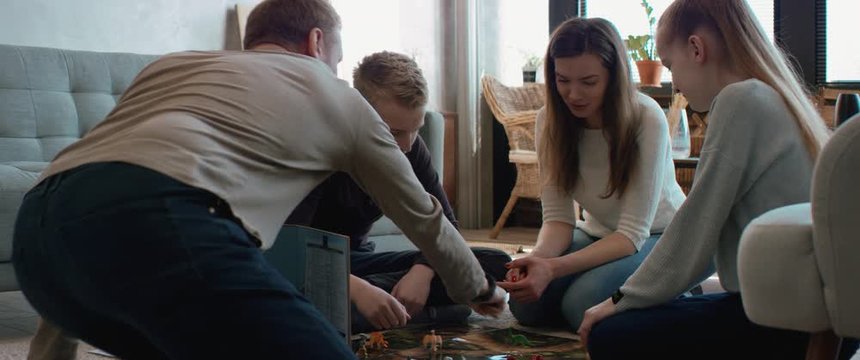 Family - father, mother and two kids playing a board game together. Stay home, quarantine. Board game is custom made for the shot. RED Dragon