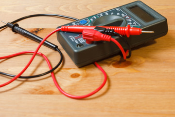 Multimeter for measuring current and voltage. Multimeter with electrodes and wires for measuring and testing volts and amps in various power sources on a wooden background