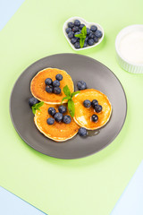 Pancakes served with fresh blueberries on gray plate over geometrical background. Healthy home made breakfast concept
