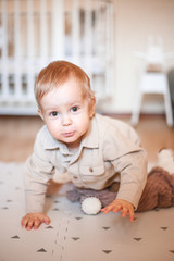 a one-year-old boy in a beige shirt and sitting on the floor