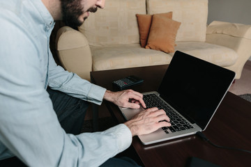 Man working online with a laptop sitting on the sofa at home. Teleworking and remote work concept