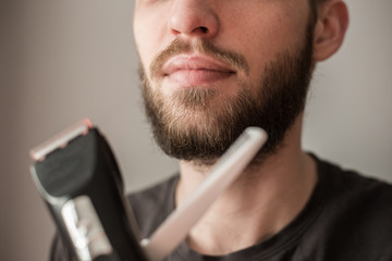 Man shaves his beard with an electric trimmer