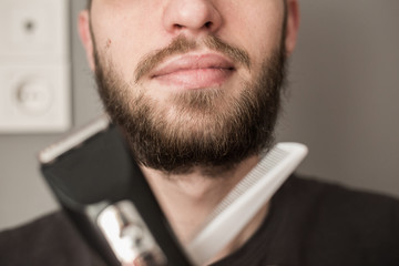 Man shaves his beard with an electric trimmer