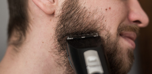 Man shaves his beard with an electric trimmer