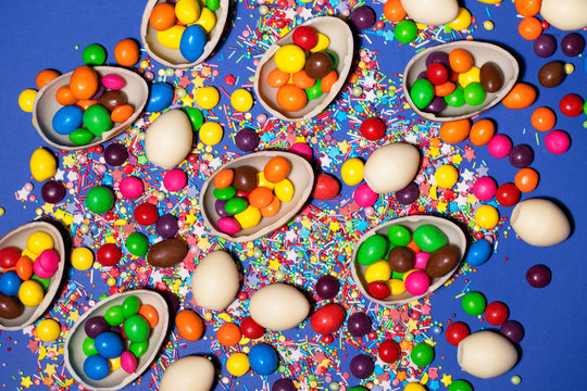 A lot of chocolate eggs, colored jellies and sweet powders were shot close-up on a dark blue background. Positive, bright photo for Easter design and any other thematic design.