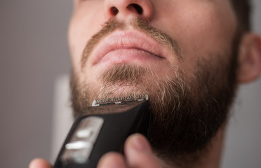 Man shaves his beard with an electric trimmer - obrazy, fototapety, plakaty