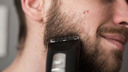 Man shaves his beard with an electric trimmer