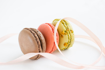 French colorful macarons with pink ribbon. Three desserts isolated close up photo.
