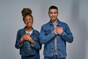 Happy girl and guy in denim jackets stand satisfied with closed eyes holding their hands on hearts....