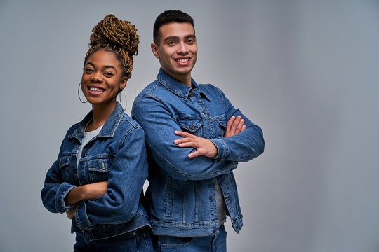 A lady and a man in denim jackets with smiles standing with their backs to each other with hands clasped on the chest. Emotions concept - Powered by Adobe