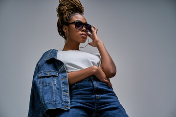 Confident lady in white t-shirt in jeans with denim jacket posing on camera in blue lighting holds hand on glasses. Fashion concept - Powered by Adobe