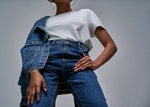Girl in white t-shirt in jeans with denim jacket posing on camera holds hands on hips. Fashion concept