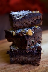 Tower of three chocolate brownies on a wooden board.  The brownies have nuts in them and have castor sugar sprinkled on the top of the brownies.