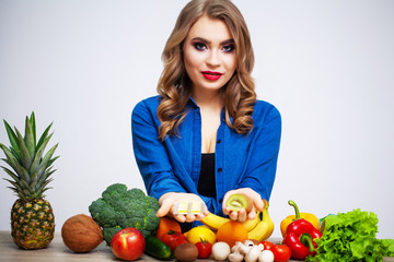 Woman at a table holding a kiwi and pills on a background of fruit and vegetables