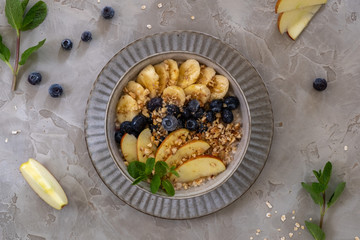 Oatmeal with blueberries, bananas, apples and chopped nuts in a beige ceramic cup