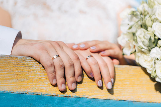 The newlyweds put their hands on a wooden railing near the bride’s white wedding bouquet.