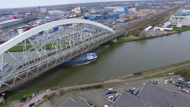 Smooth aerial drone shot of an industrial cargo ship cruising under a bridge and trough the water of the canal 4K