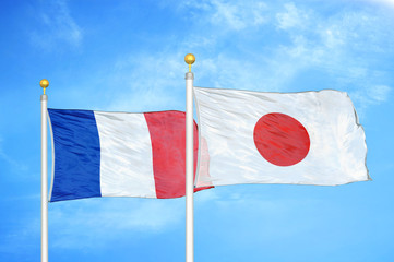 France and Japan two flags on flagpoles and blue cloudy sky
