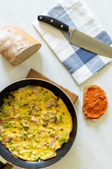 Flat lay above omelet in the frying pan with bread knife and ajvar on the bread