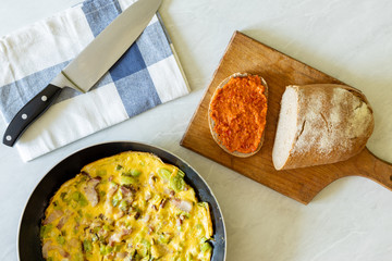 Flat lay above omelet in the frying pan with bread knife and ajvar on the bread