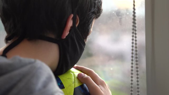 The boy with black mask and ball. Isolation time. The boy looks sadly out the window. Corona virus. Covid-19.