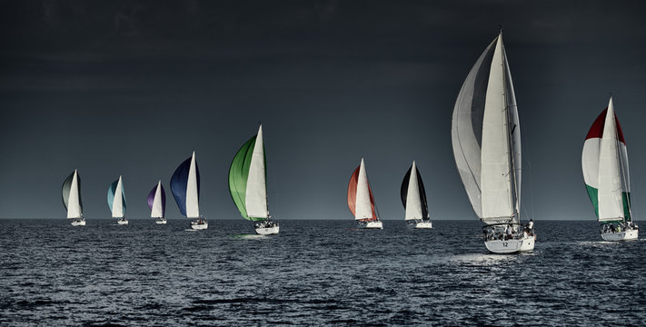Sailboats compete in a sailing regatta at sunset, sailing race, reflection of sails on water, multi-colored spinaker, boat number aft boats, big white clouds,