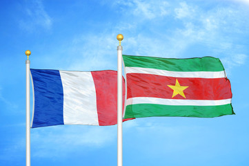 France and Suriname two flags on flagpoles and blue cloudy sky