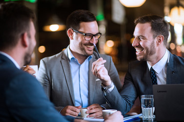 Three smiling businessmen in formal wear talking in cafe