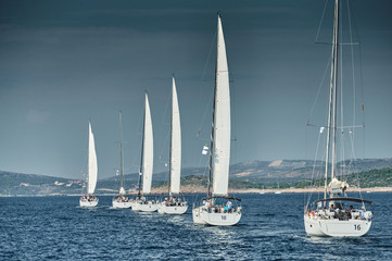 Fototapeta na wymiar Sailboats compete in a sailing regatta at sunset, sailing race, reflection of sails on water, multi-colored spinaker, boat number aft boats, big white clouds,