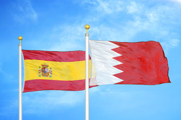 Spain and Bahrain  two flags on flagpoles and blue cloudy sky