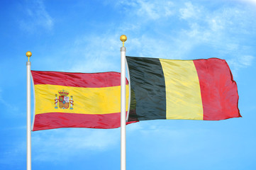 Spain and Belgium  two flags on flagpoles and blue cloudy sky