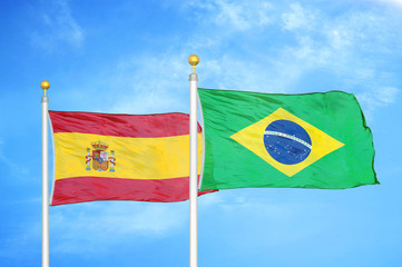 Spain and Brazil  two flags on flagpoles and blue cloudy sky