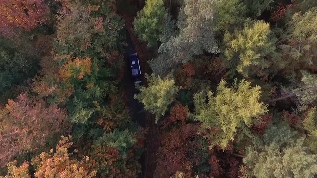 Cinematic aerial drone shot of a camper van driving trough a beautiful orange and red colored autumn forest 