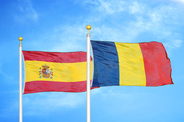 Spain and Chad  two flags on flagpoles and blue cloudy sky