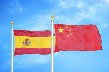 Spain and China two flags on flagpoles and blue cloudy sky
