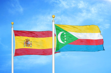 Spain and Comoros two flags on flagpoles and blue cloudy sky