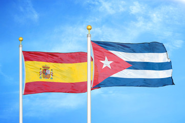 Spain and Cuba two flags on flagpoles and blue cloudy sky