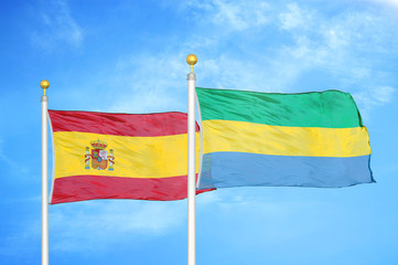 Spain and Gabon two flags on flagpoles and blue cloudy sky
