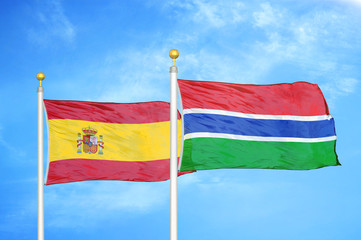 Spain and Gambia two flags on flagpoles and blue cloudy sky