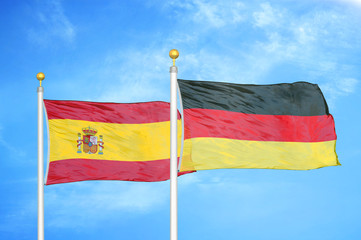Spain and Germany two flags on flagpoles and blue cloudy sky