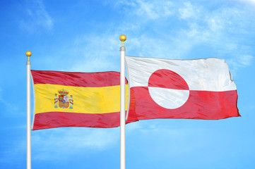 Spain and Greenland two flags on flagpoles and blue cloudy sky