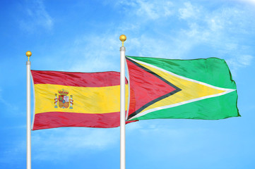 Spain and Guyana two flags on flagpoles and blue cloudy sky