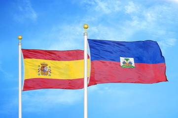 Spain and Haiti two flags on flagpoles and blue cloudy sky