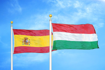 Spain and Hungary two flags on flagpoles and blue cloudy sky