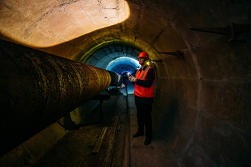 Tunnel worker examines pipeline in underground tunnel