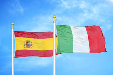 Spain and Italy two flags on flagpoles and blue cloudy sky
