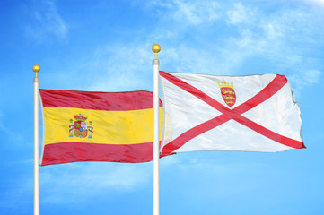 Spain and Jersey two flags on flagpoles and blue cloudy sky