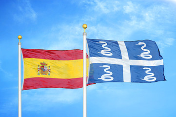 Spain and Martinique snake two flags on flagpoles and blue cloudy sky