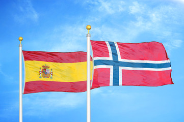 Spain and Norway two flags on flagpoles and blue cloudy sky
