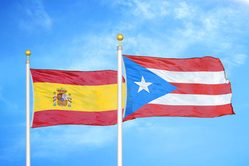 Spain and Puerto Rico two flags on flagpoles and blue cloudy sky